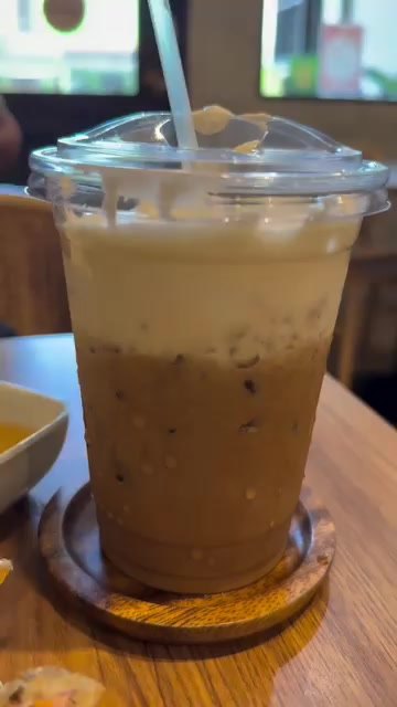 Iced Vietnamese coffee with a creamy top on a wooden coaster