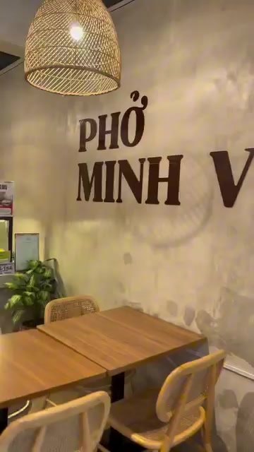 Dining room with wooden tables, rattan chairs, woven lamps and the Phở Minh Vũ name on the wall