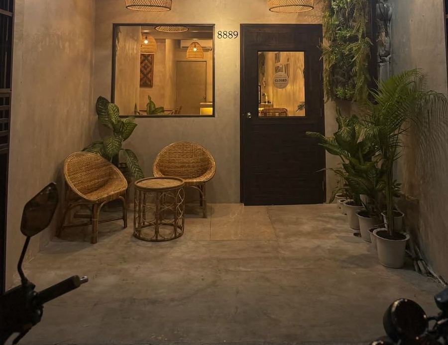Entrance of the Phở Minh Vũ Makati branch with a dark wooden door, two rattan chairs and potted plants